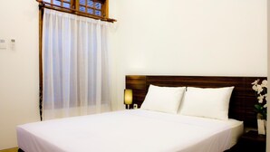A neatly made bed with white linens, a wooden headboard, and a bedside table with a lamp. - Grand Marto Hotel (Yogyakarta)