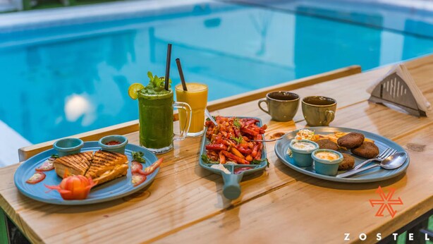 Bandeja de desayuno con queso a la plancha, un batido verde, ensalada de frutas y galletas junto a una piscina.