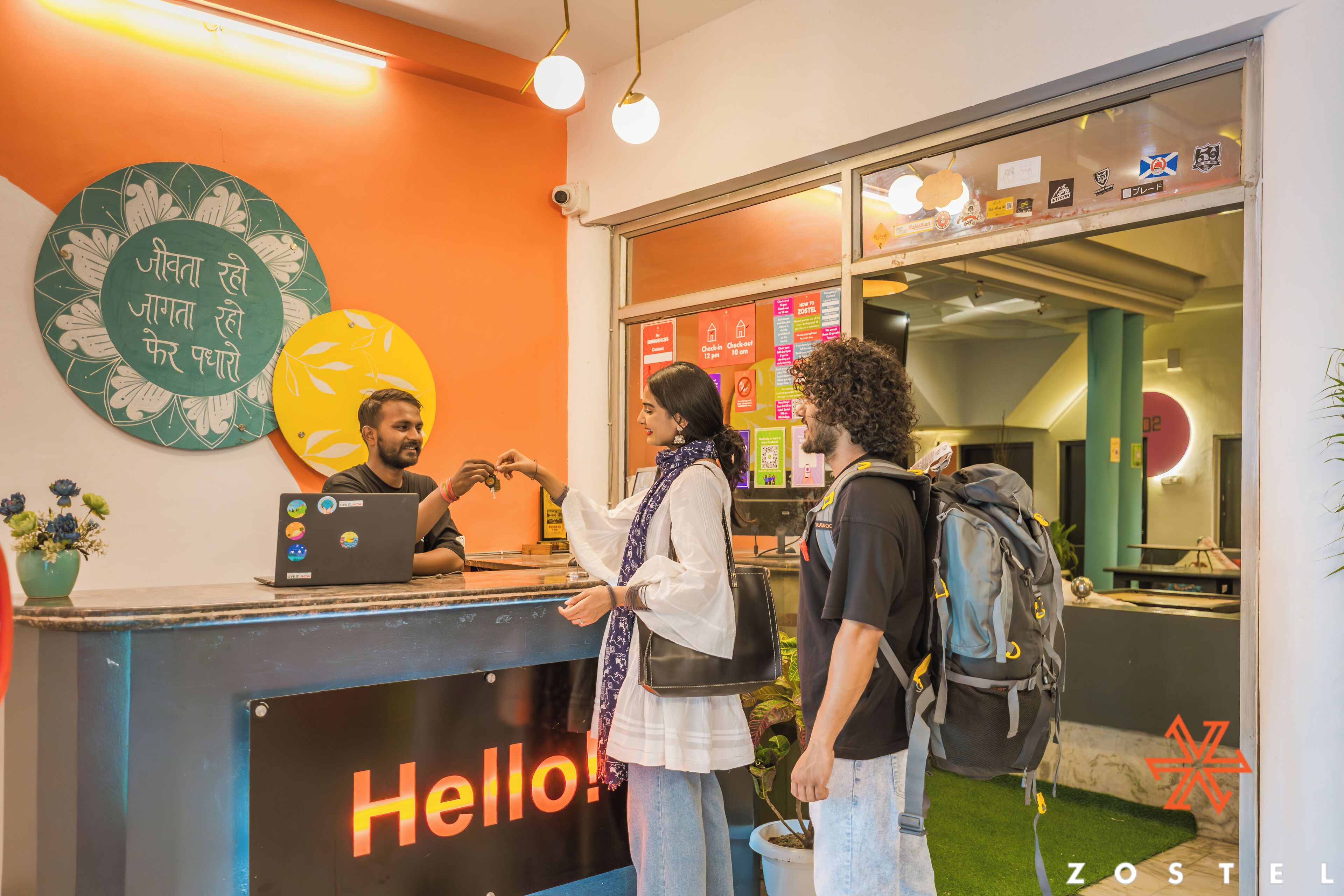 Una reception con un cartello che riporta 'Hello!', un portatile e una persona che parla con un membro dello staff.