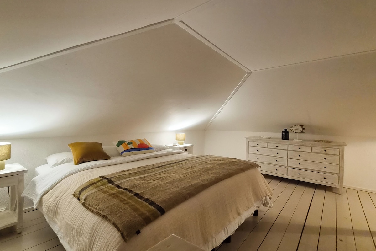 Un dormitorio con cama, mesitas de noche, cómoda y lámpara.
