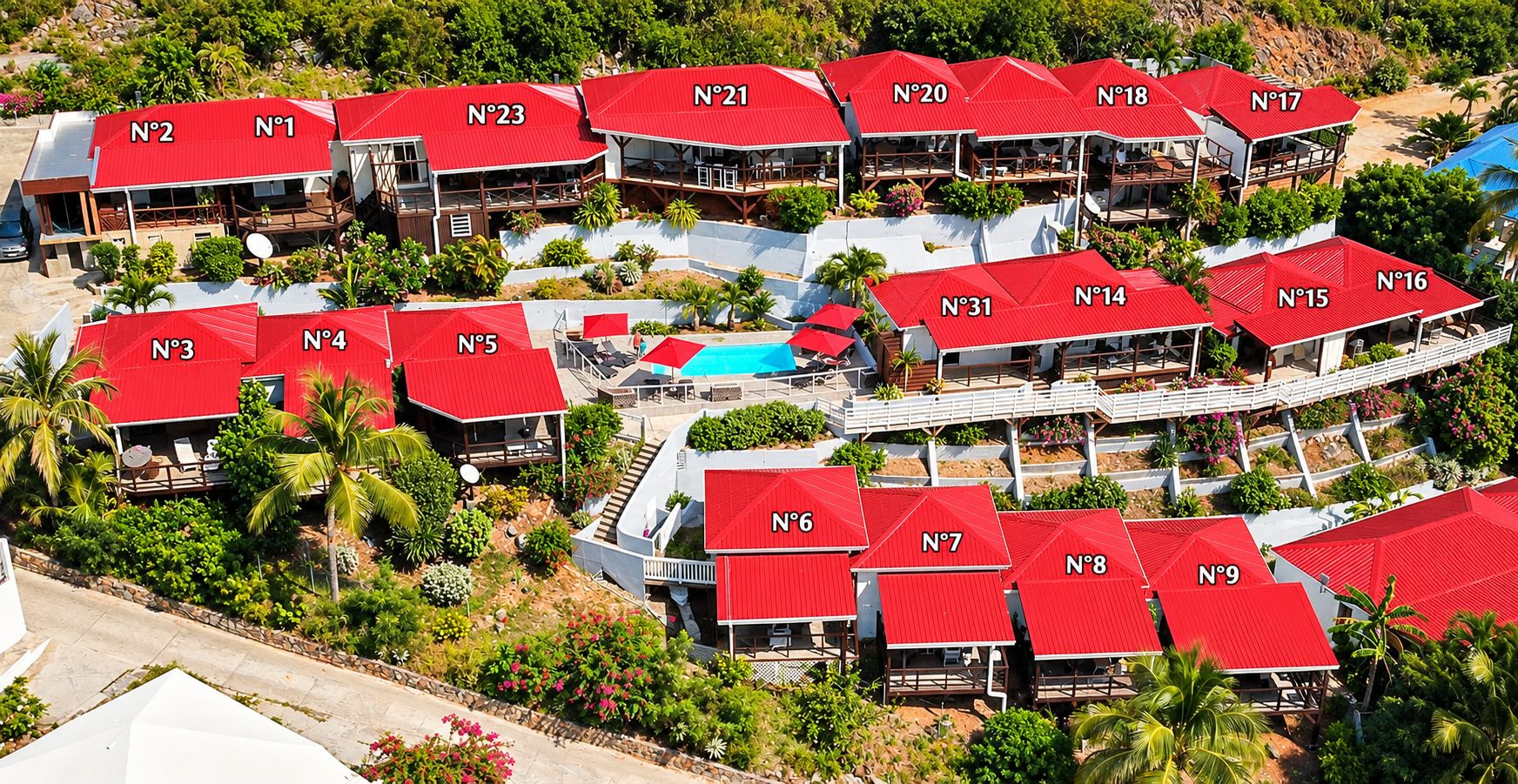 Un resort con varios edificios de techo rojo, algunos con balcones, rodeado de vegetación y una zona de piscina.