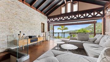 Un salon moderne avec un mur en pierre, des poutres en bois, un canapé, une table basse en verre et une vue sur un lac.