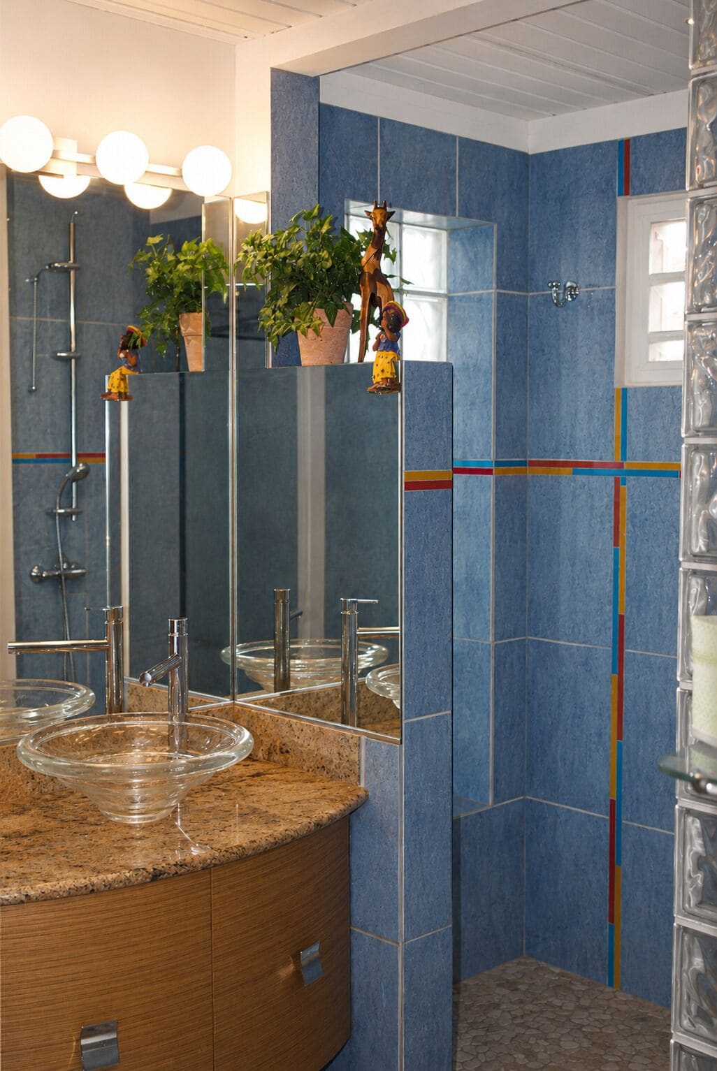A bathroom with a granite countertop, a glass sink, a mirror, and a shower area.
