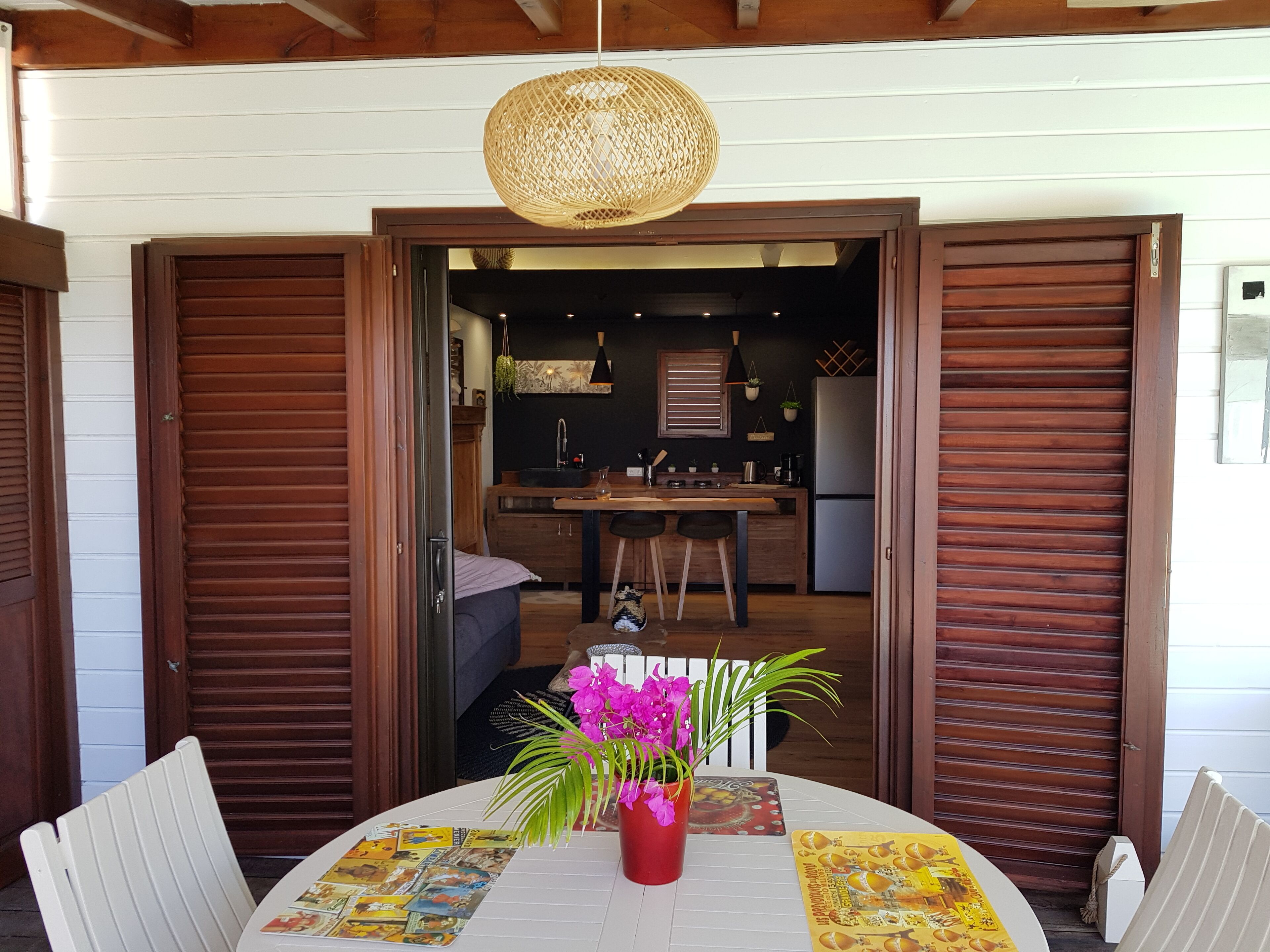 A dining area with a round table, chairs, a hanging light fixture, and a view into the kitchen.