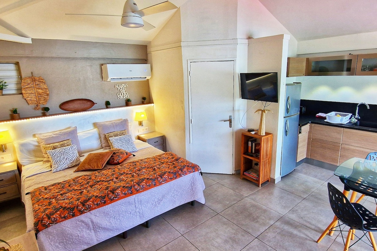 Un dormitorio moderno con cama, mesitas de noche, una lámpara de noche, TV montada en la pared y una pequeña estantería con objetos decorativos.