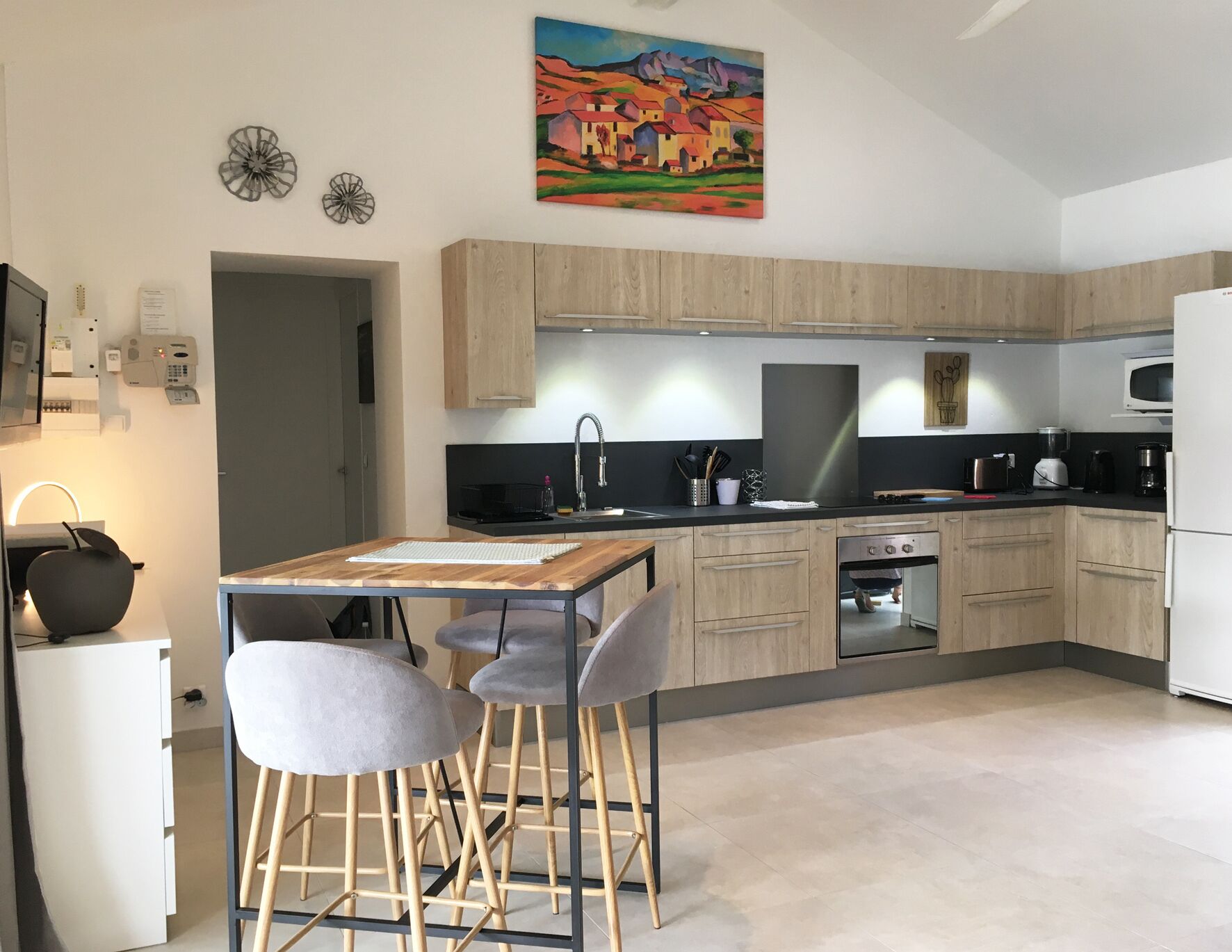 Une cuisine moderne avec des meubles en bois, un plan de travail noir et un coin repas comprenant une table et deux chaises.