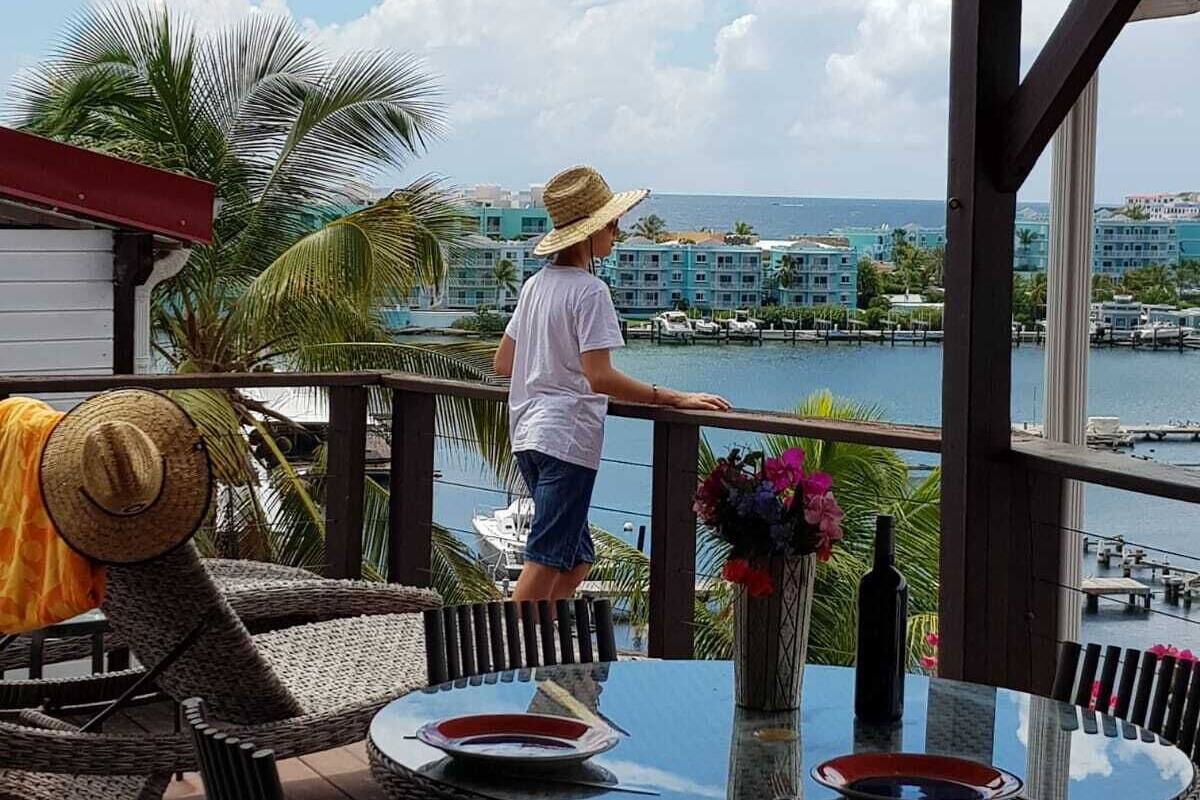 A balcony with a view of the sea, a table with chairs, and a person standing by the railing.