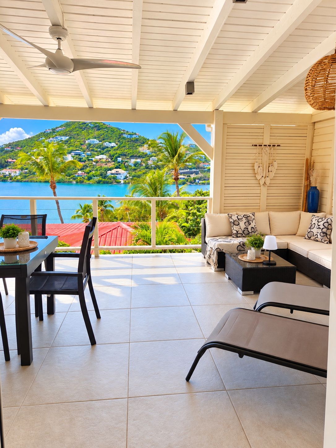 A covered outdoor seating area with a view of a coastal landscape, including houses and palm trees.