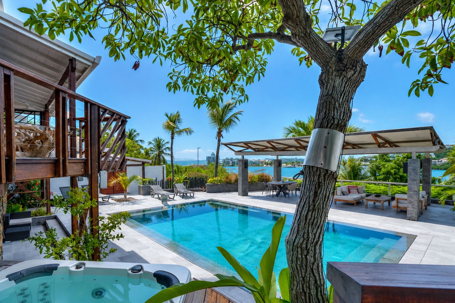 A pool area with lounge chairs, a hot tub, and a view of the ocean.