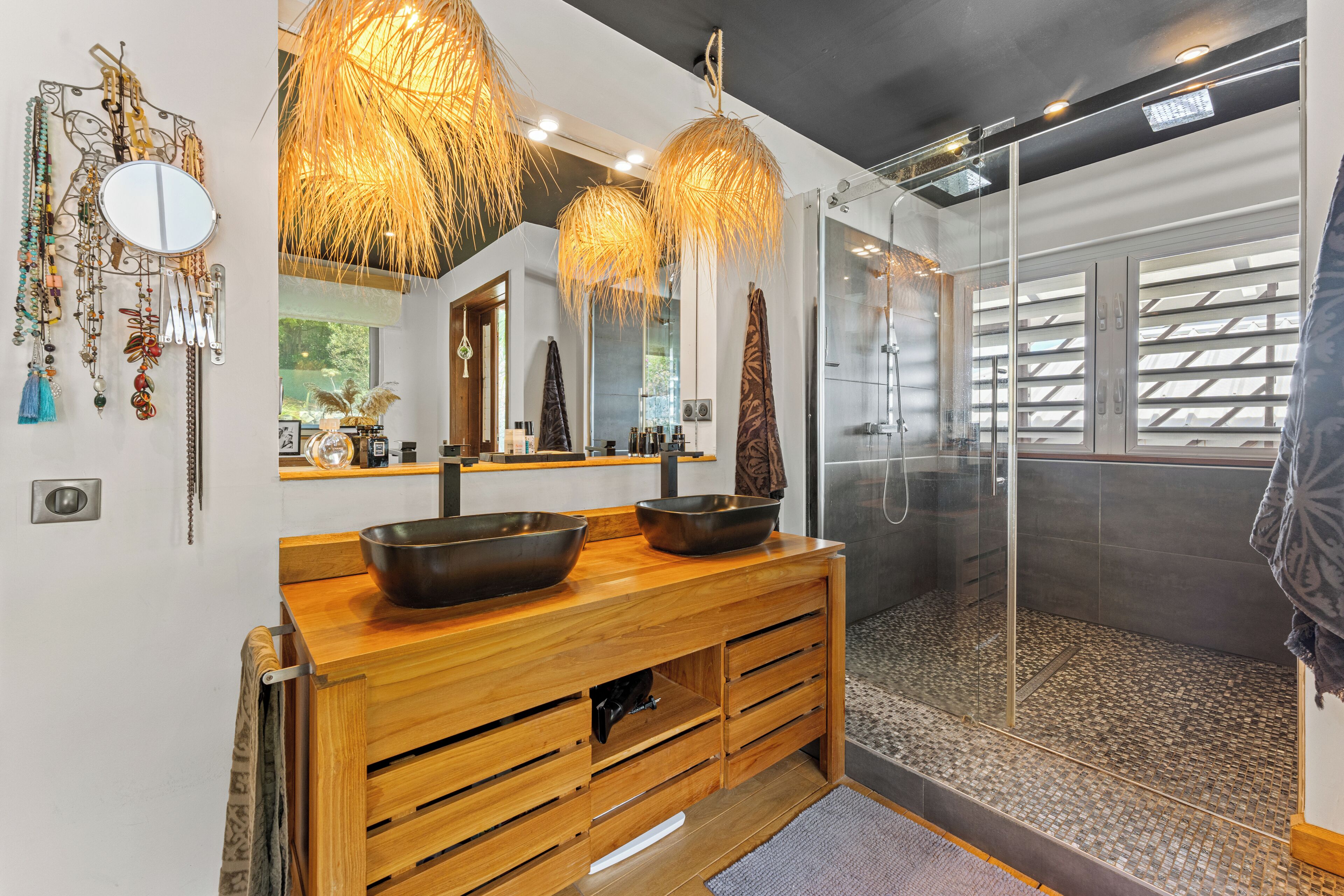 A modern bathroom with a wooden vanity, a large mirror, and a glass shower enclosure.