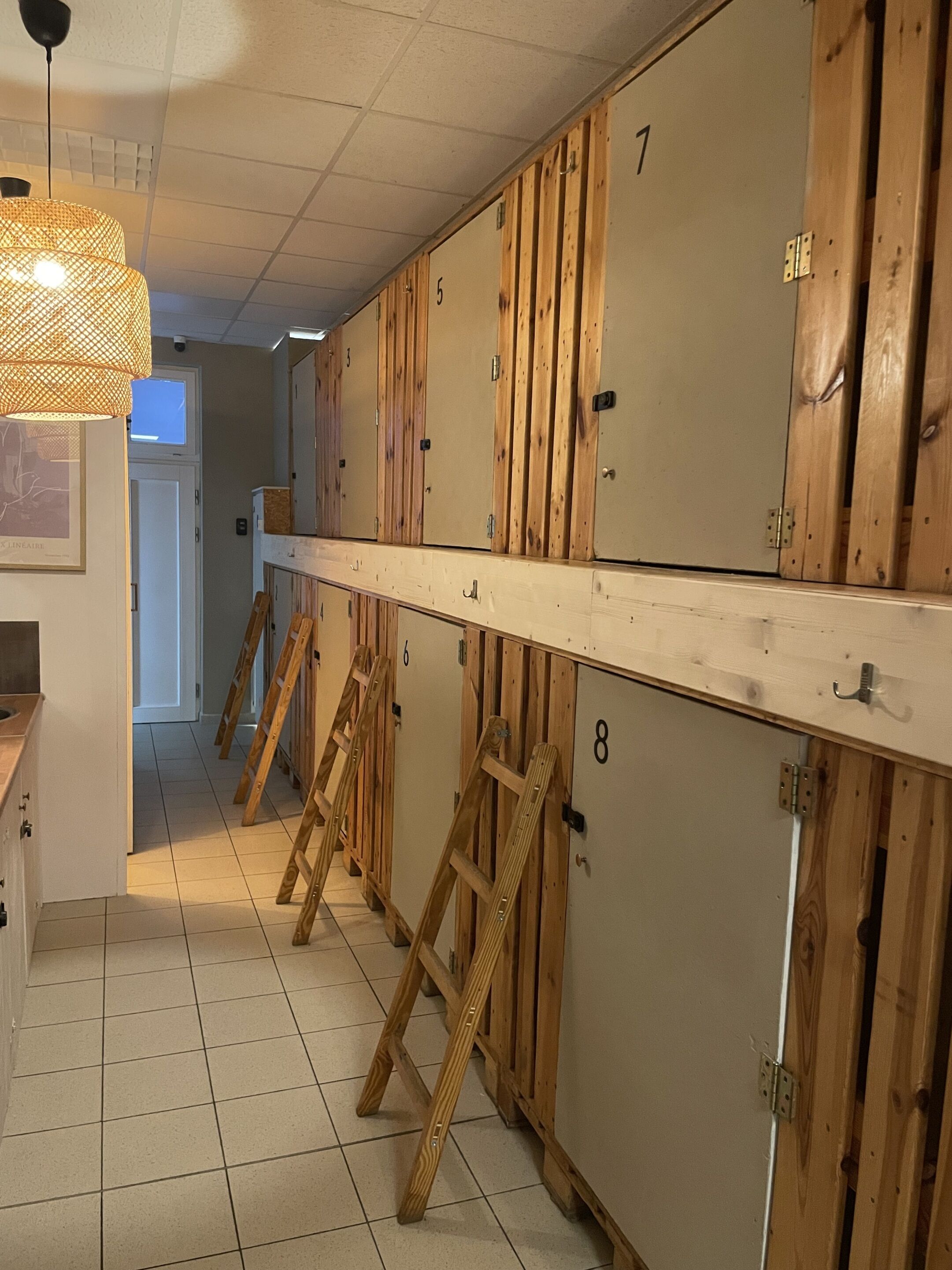 A row of wooden lockers with numbers, a tiled floor, and a hanging light fixture.
