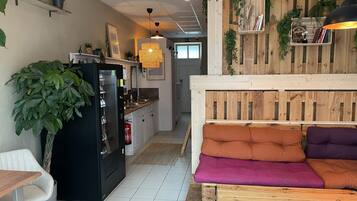 Una cocina moderna con refrigerador integrado, un comedor con una silla blanca y una sala de estar con un banco de madera y cojines.