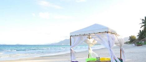Uma praia com uma tenda branca e cadeiras de descanso coloridas.