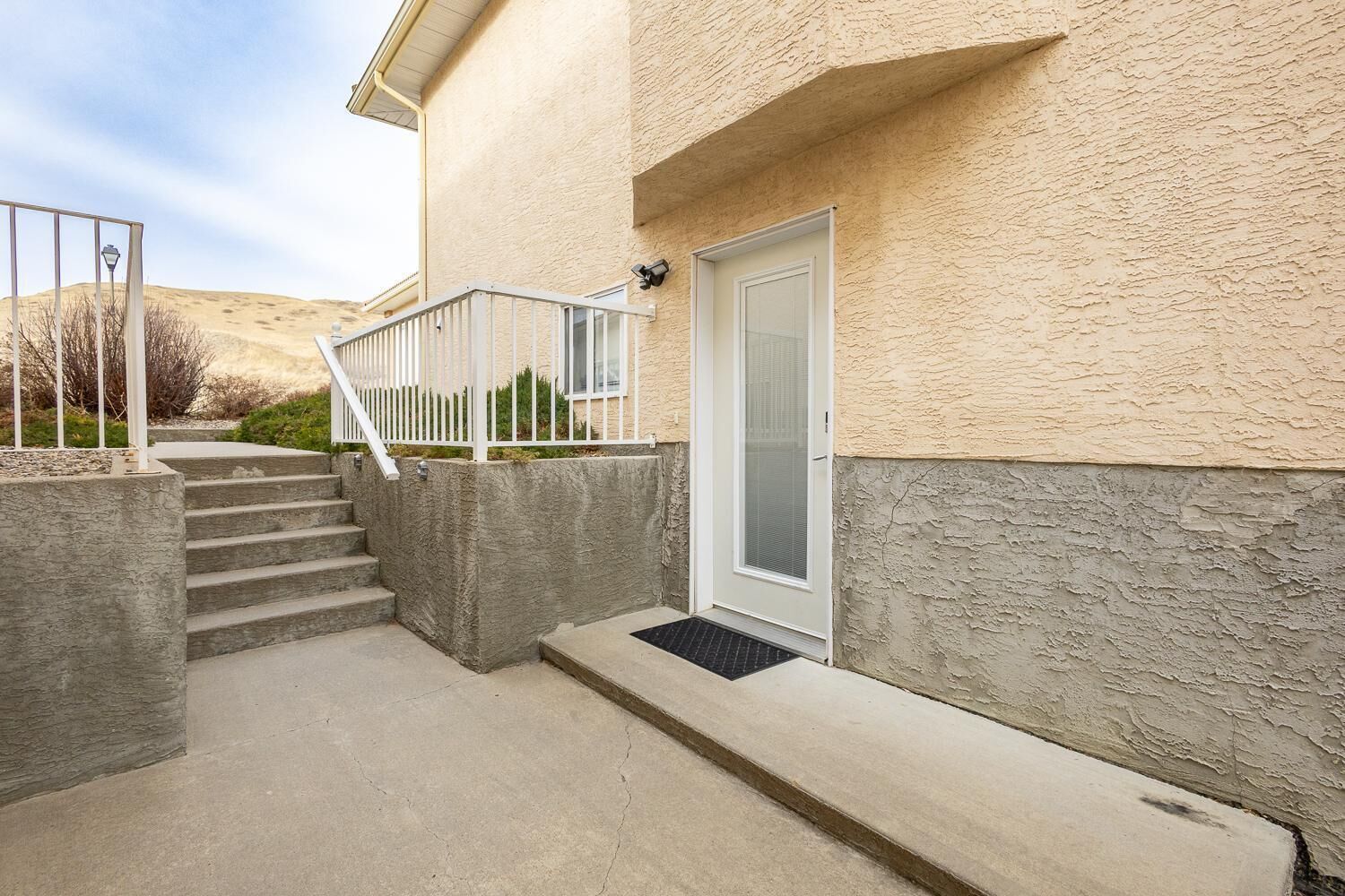 A residential building with a concrete staircase leading to a door, a small porch area, and a security camera.