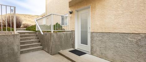 A residential building with a concrete staircase leading to a door, a small porch area, and a security camera.