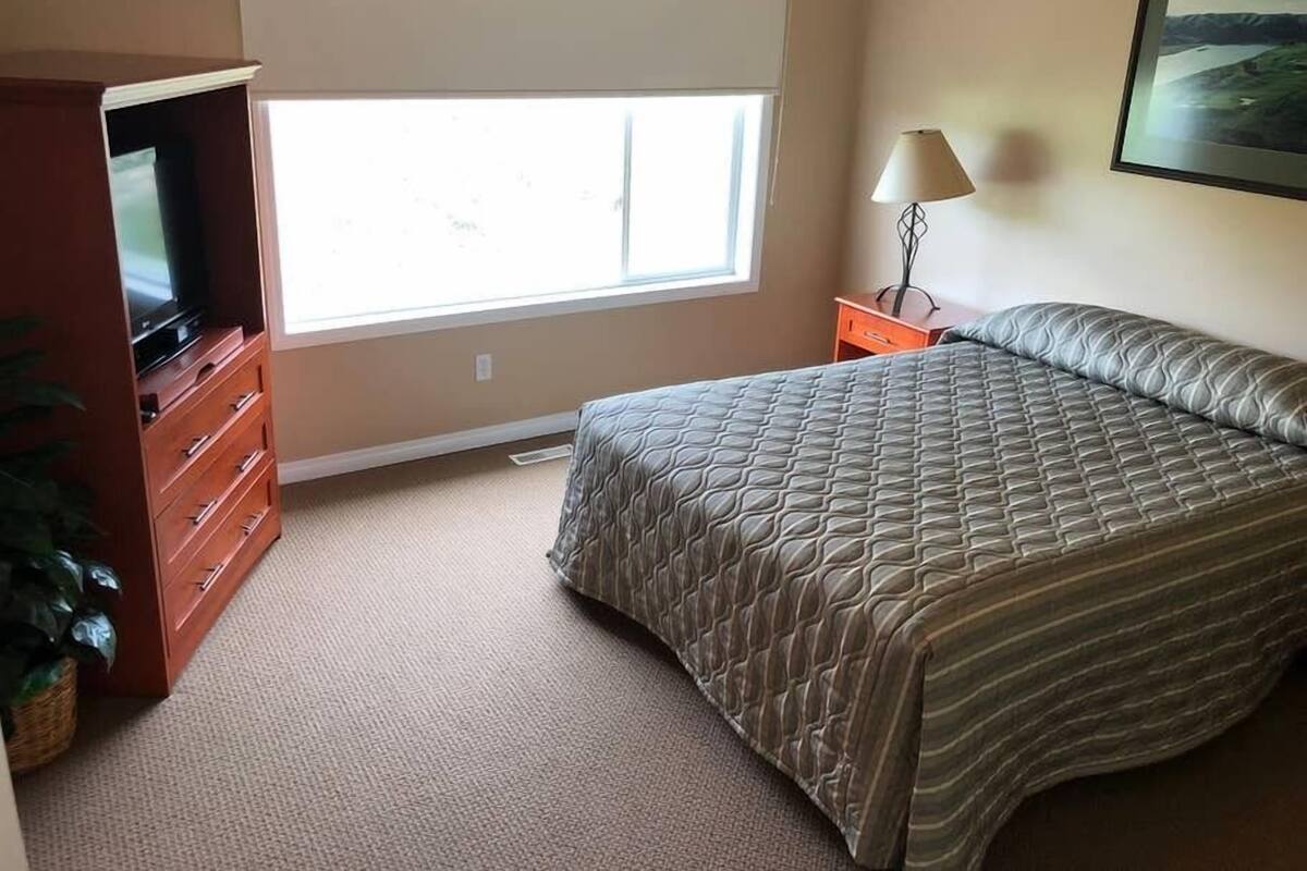 A bedroom with a bed, a dresser, a TV, a lamp, and a window.