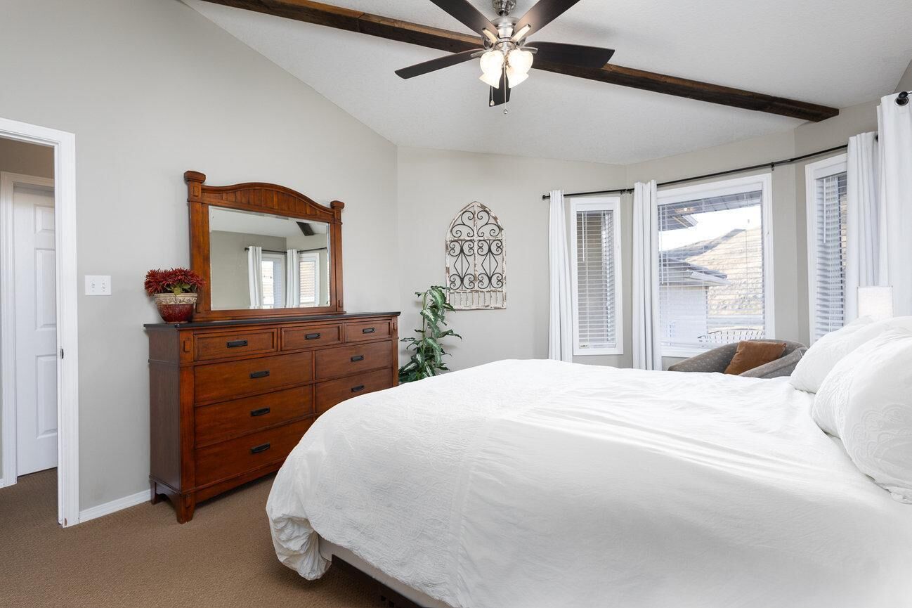 Een slaapkamer met een groot bed, een houten dressoir, een plafondventilator en een raam met zonwering.