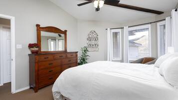 Een slaapkamer met een groot bed, een houten dressoir, een plafondventilator en een raam met zonwering.