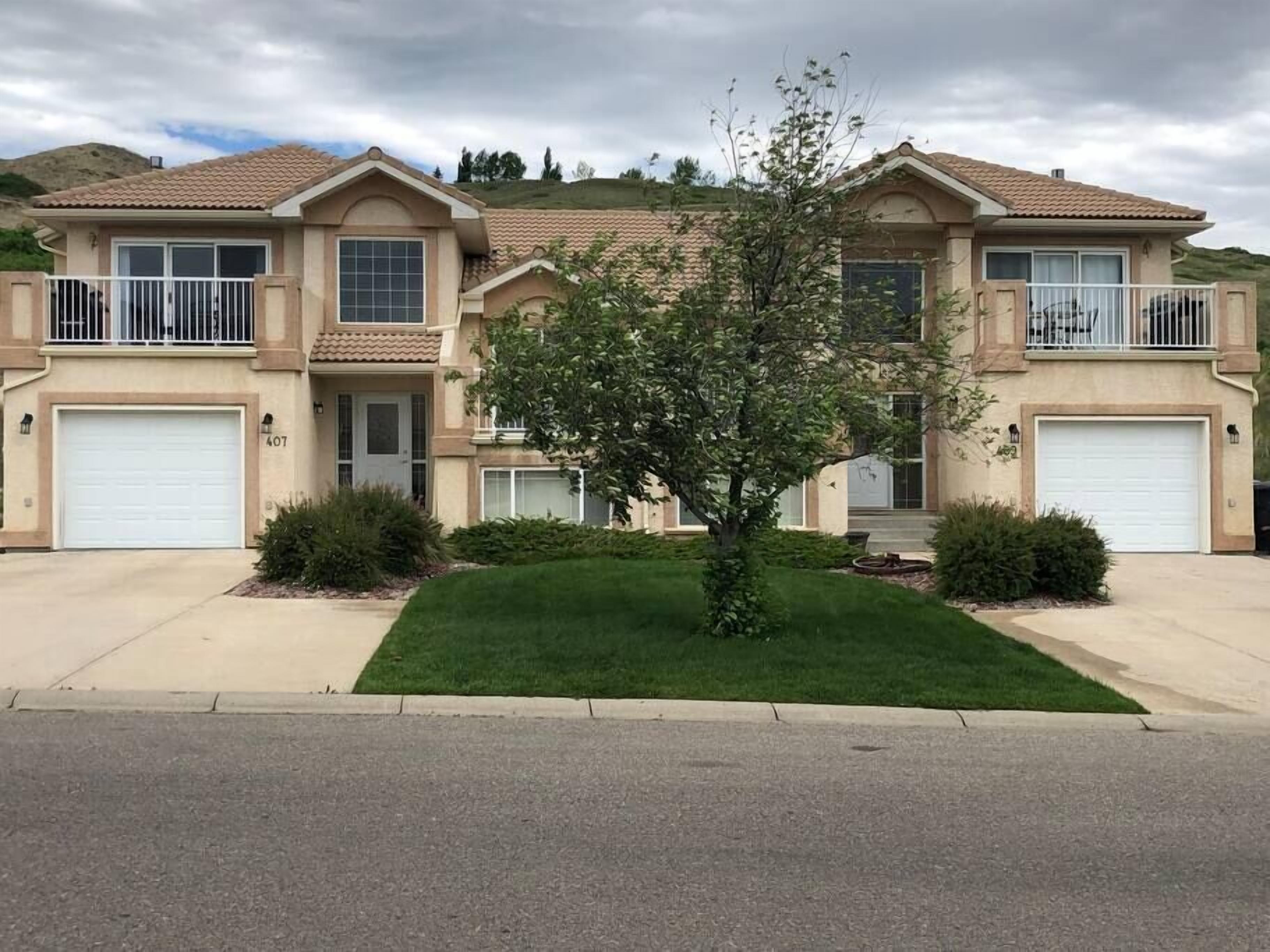 Una casa residencial de dos pisos con jardín delantero, un árbol pequeño y un garaje.