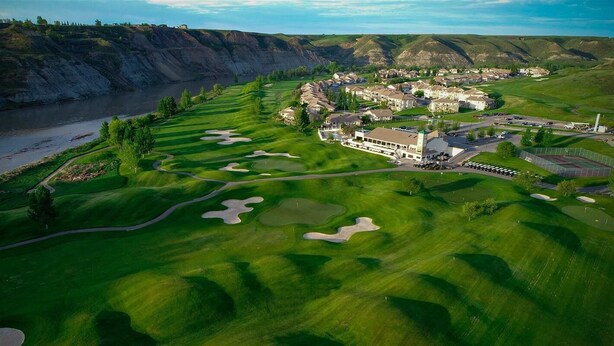 An aerial view of a golf course with a clubhouse, sand bunkers, and a river. - Paradise Canyon Golf Resort (Lethbridge)