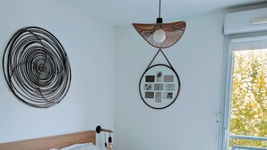 A neatly made bed with patterned bedding, a wall-mounted circular decoration, a hanging light fixture, and a window with a view of trees. - F2 garage,terrace,wifi,near town hall/train station/richter (Montpellier)