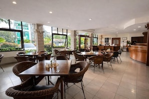 A spacious indoor area with multiple dining tables and chairs, large windows offering a view of the outside, and a reception desk.
