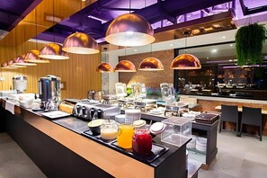 Zona de bufé con diversos alimentos y bebidas, incluyendo una cafetera, tostadoras y una barra de ensaladas.