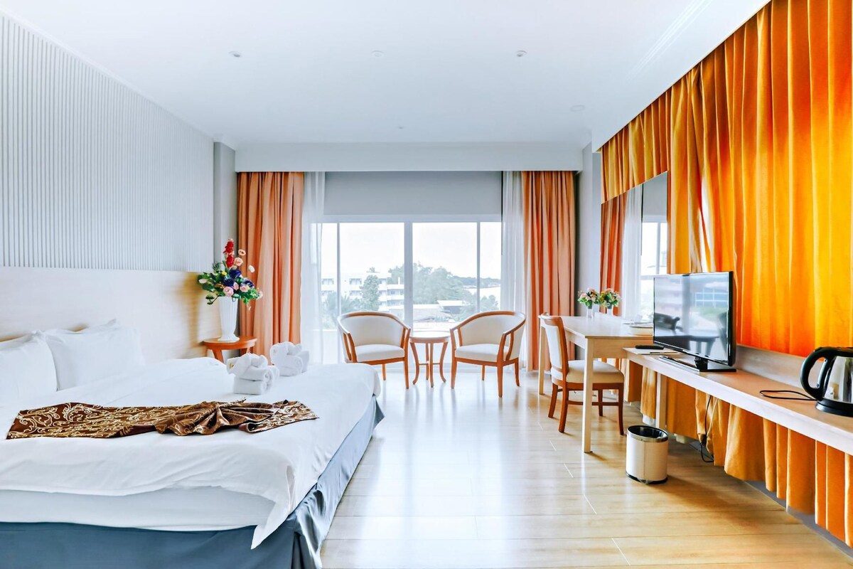A hotel room with a bed, a desk with a television, a chair, and a view of the city.
