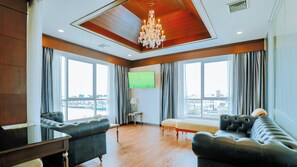 A spacious living room with a wooden ceiling, a chandelier, leather sofas, a TV, and large windows with a city view. - CBD 2 Hotel (Surat Thani)