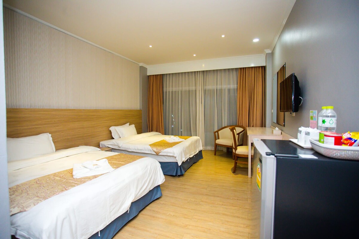 A hotel room with two beds, a desk, a chair, a television, and a minibar.