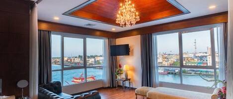 Quarto de hotel com uma grande janela, um candelabro, um sofá, um banco e uma TV de tela plana.