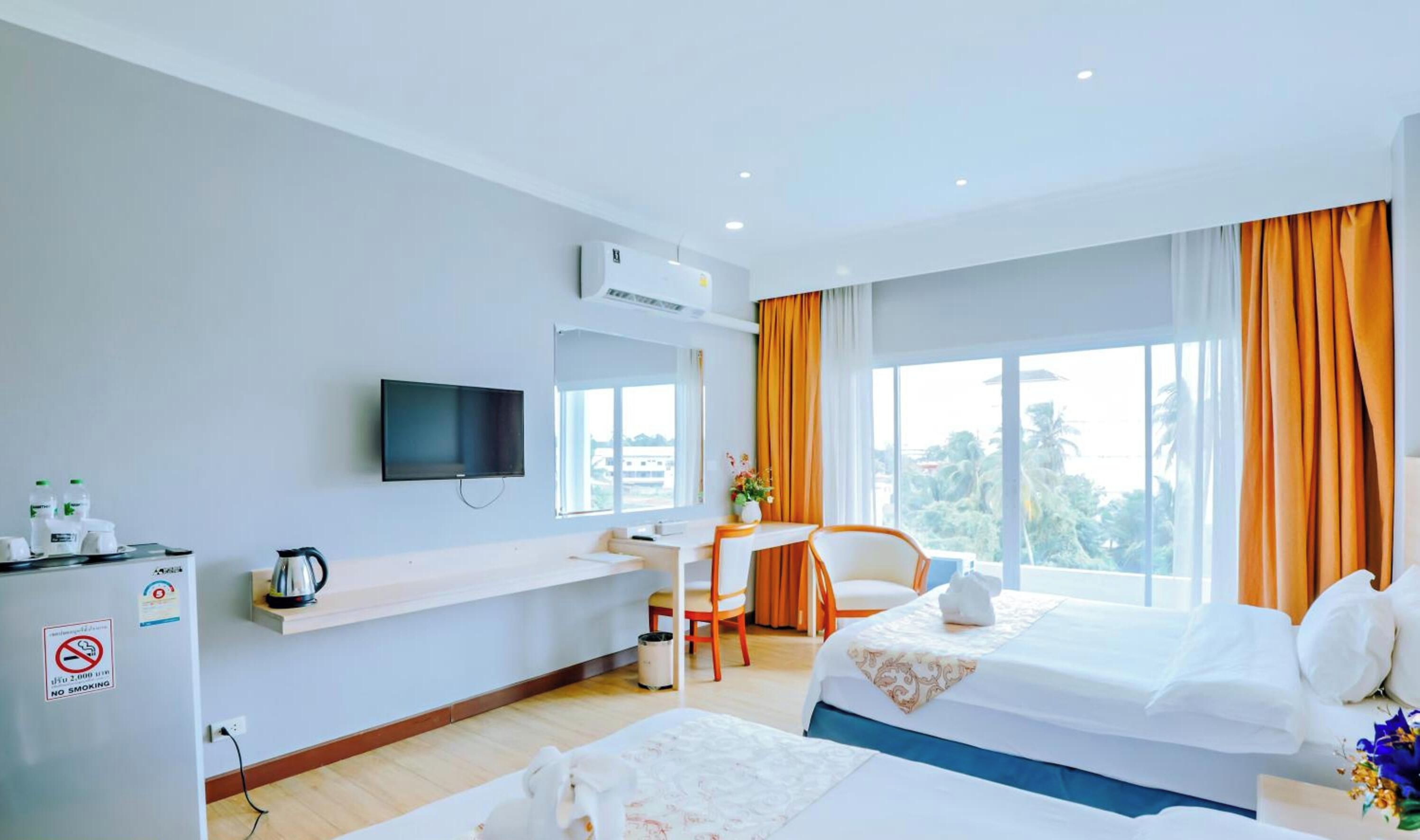 A hotel room with a bed, a desk with a chair, a television, and a window with curtains.