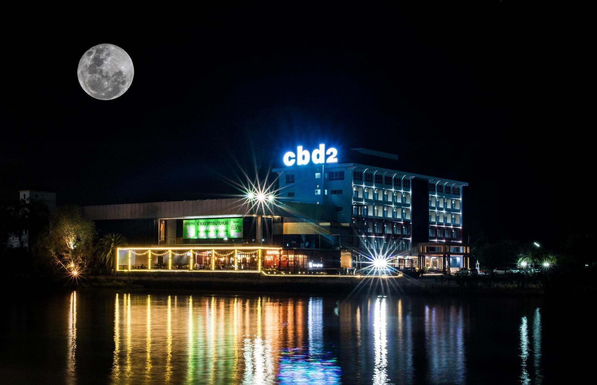 A hotel with a 'cbd2' sign, a reflection in the water, and a full moon in the sky.