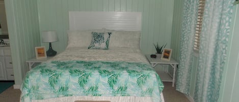 Een slaapkamer met een bed, nachtkastjes, een bankje en een raam met gordijnen.