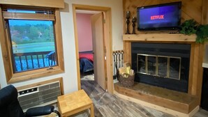 A cozy living room with a fireplace, a television displaying 'NETFLIX', and a view through a window.