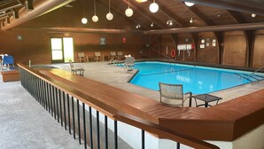 An indoor swimming pool with a wooden deck, chairs, and a lifeguard chair.