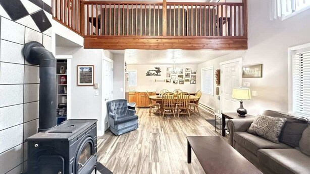A spacious living area with a high ceiling, a wooden staircase, a fireplace, a dining table with chairs, and a sofa.