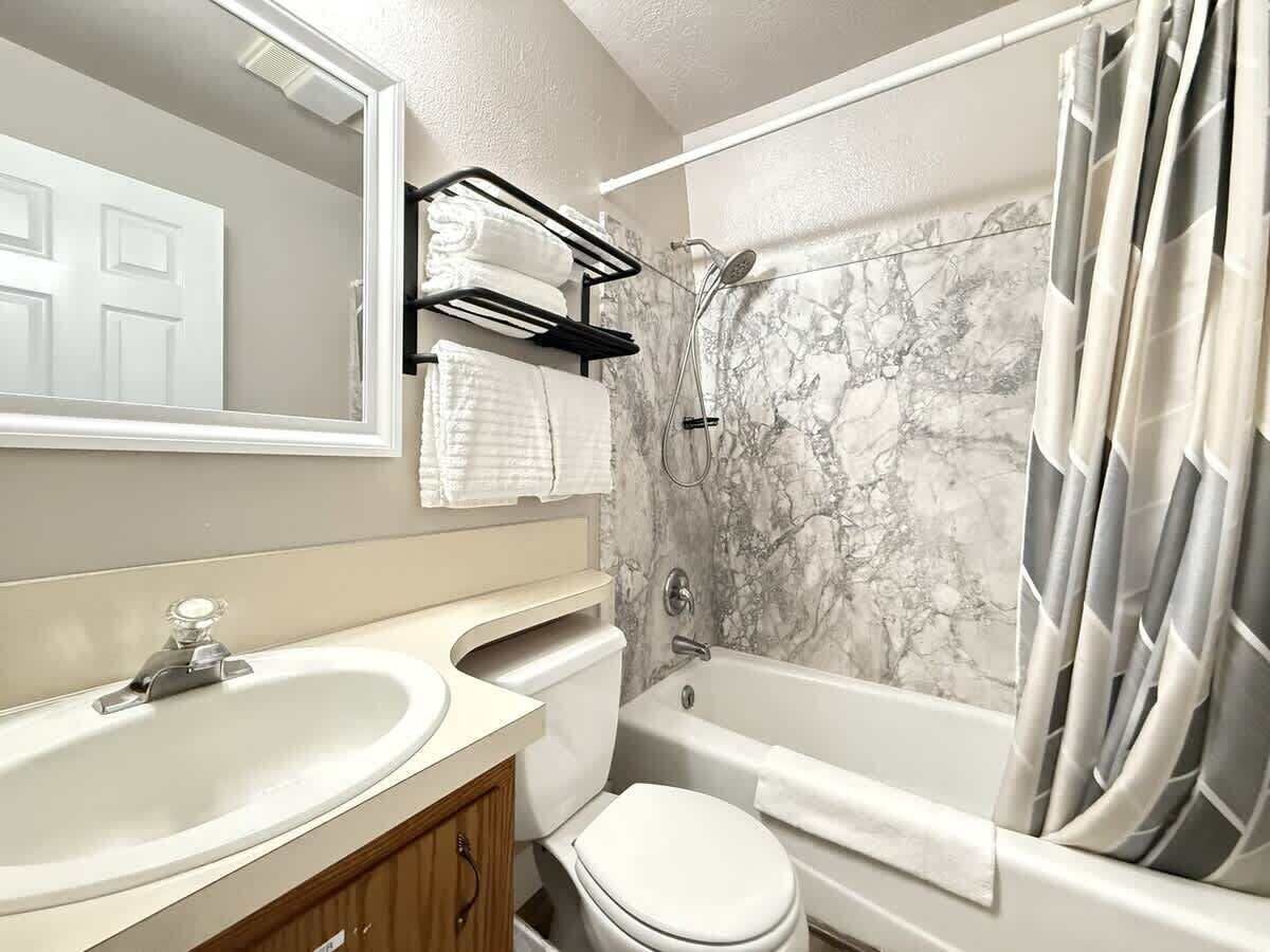 A bathroom with a marble wall, a bathtub, a toilet, and a sink.