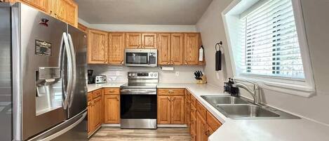A modern kitchen with wooden cabinets, stainless steel appliances, and a window providing natural light.