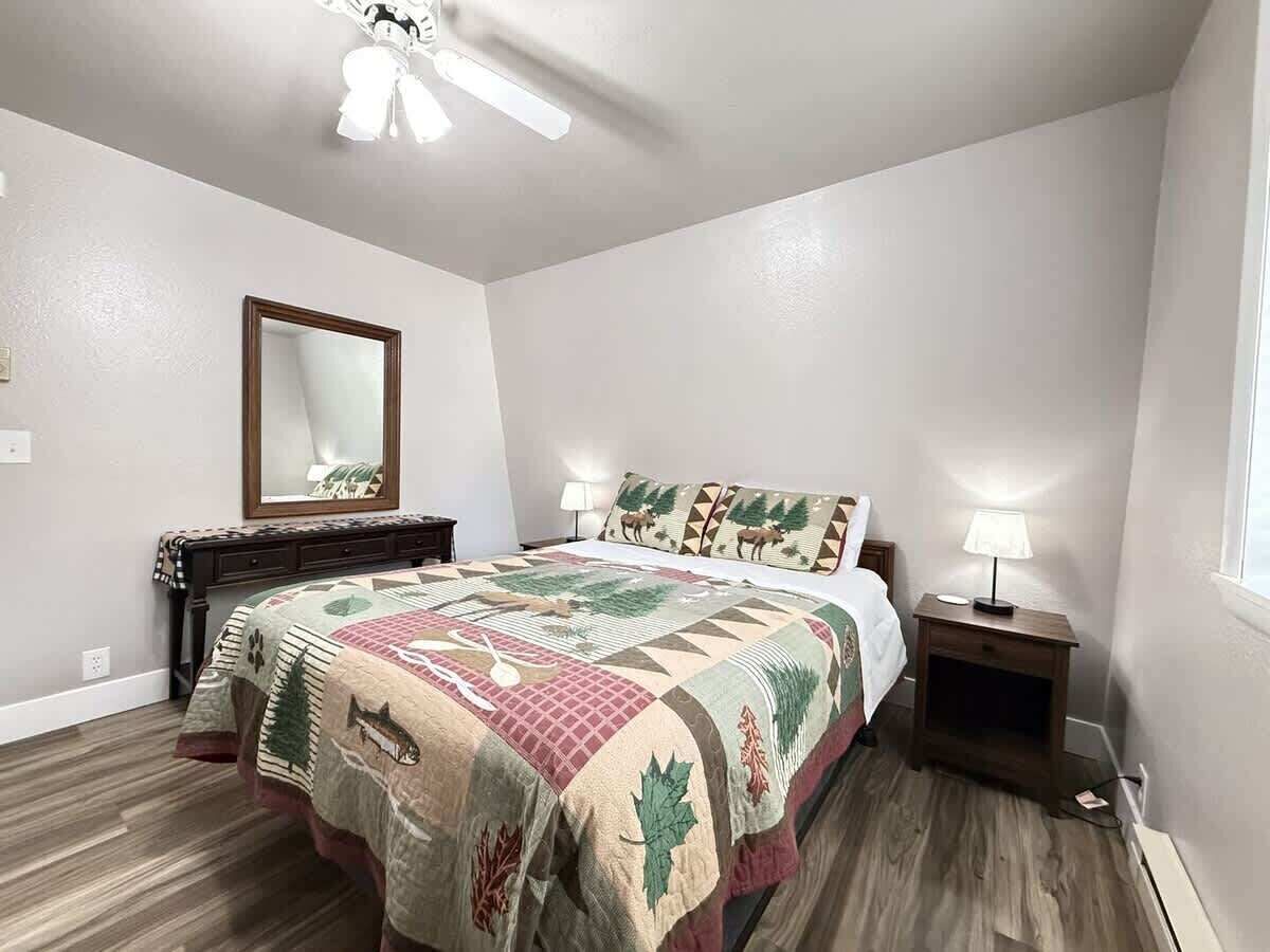 Een slaapkamer met een bed, nachtkastje, lamp, spiegel en plafondventilator.