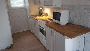 Uma cozinha compacta com armários brancos, bancada de madeira, forno embutido e micro-ondas.
