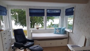 Um quarto com um amplo assento junto à janela, uma cadeira preta, uma mesinha e um aparador branco.