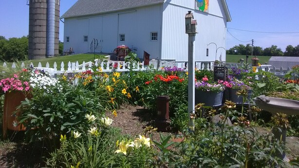 A white barn with a colorful mural, surrounded by a white picket fence and a variety of flowers. -  Bloomin Pickets Farmhouse Stay OR Ladies Craft Retreat! (Monroe)