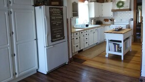 A kitchen with white cabinets, a refrigerator, a sink, and a wooden island. There is a welcome sign on the refrigerator. -  Bloomin Pickets Farmhouse Stay OR Ladies Craft Retreat! (Monroe)