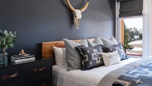 A bedroom with a bed, a dresser, a wall-mounted skull, a window with a view, and a ceiling fan. - The Village at Palisades Tahoe Bldg 1 - Chic Condo with Prime View (Olympic Valley)