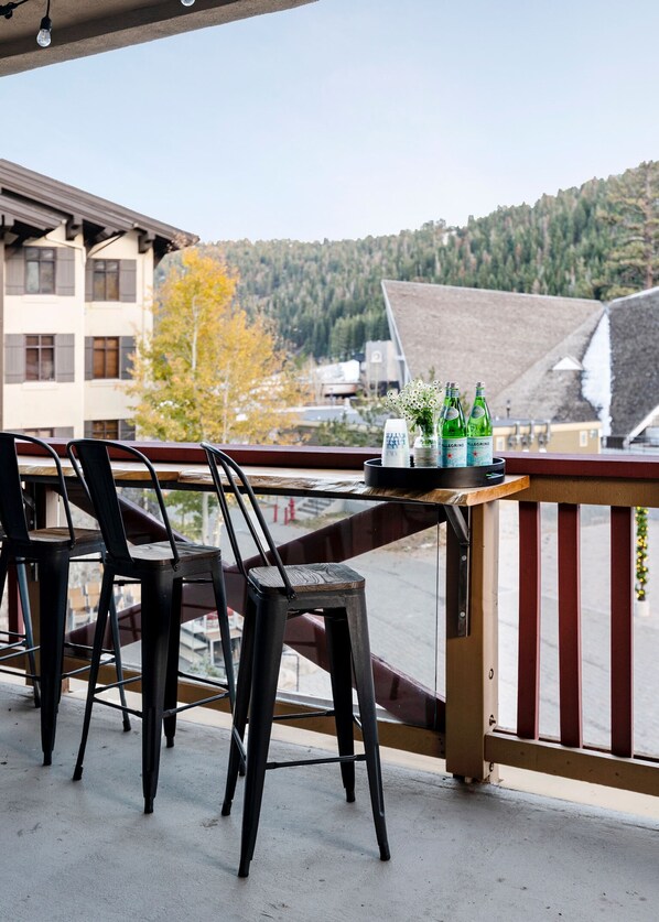 A balcony with two chairs and a table, overlooking a residential area with trees and buildings. - The Village at Palisades Tahoe Bldg 1 - Chic Condo with Prime View (Olympic Valley)