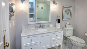 A bathroom with a white vanity, a sink, a toilet, and a shower area. - The West Lane Inn - King Room (Ridgefield)