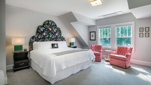 A bedroom with a large bed, two nightstands, a window with a view, and a red armchair. - The West Lane Inn - King Room (Ridgefield)