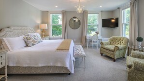 A bedroom with a large bed, a desk, a chair, a television, and a window with curtains. - The West Lane Inn - King Room (Ridgefield)