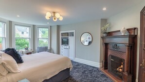 A bedroom with a large bed, a fireplace, a mirror, and a desk with a chair. - The West Lane Inn - Deluxe Fireplace King (Ridgefield)